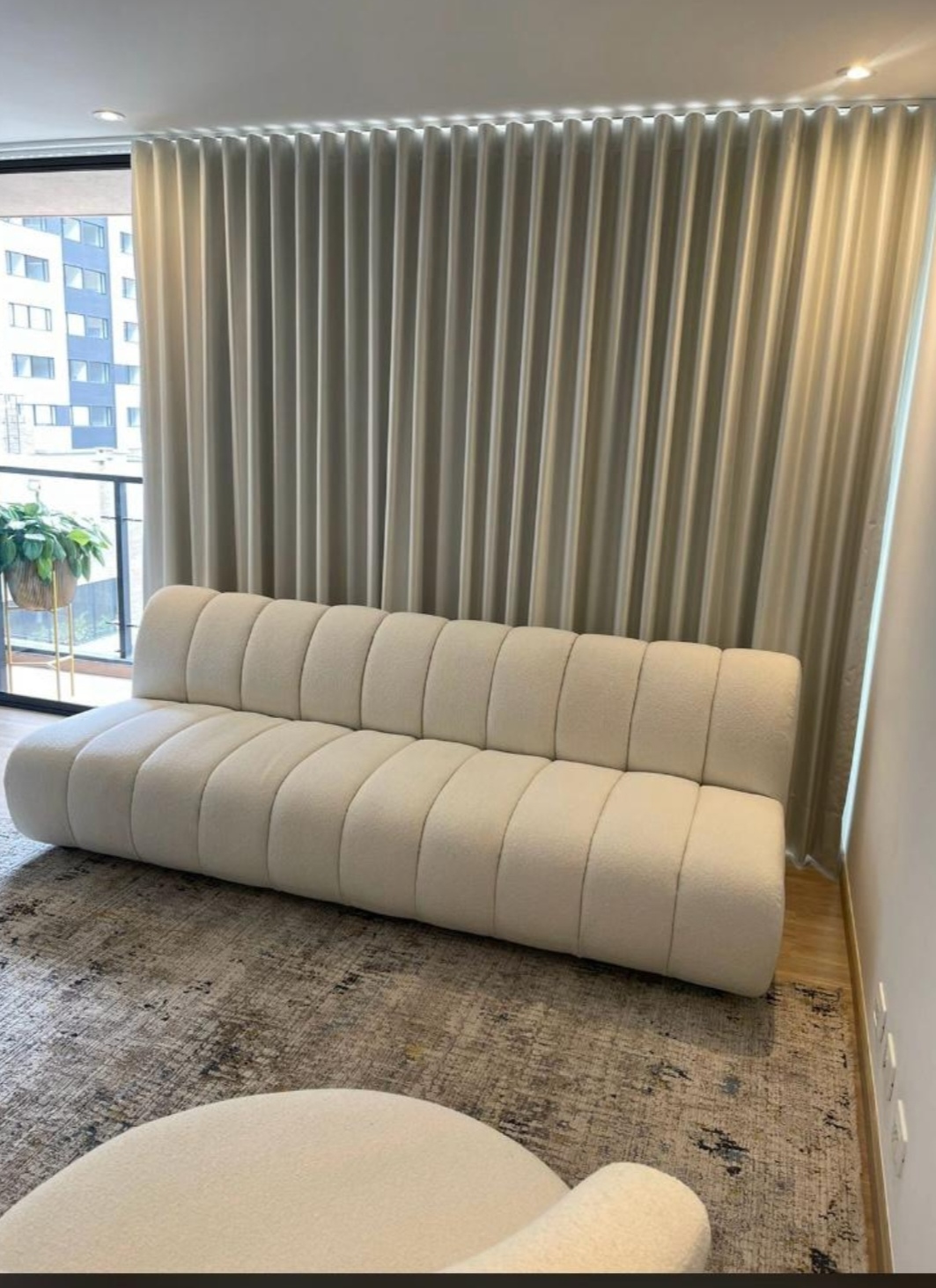 Sala con sofá modular en bouclé crema frente a cortinas de piso a techo con luz cálida integrada